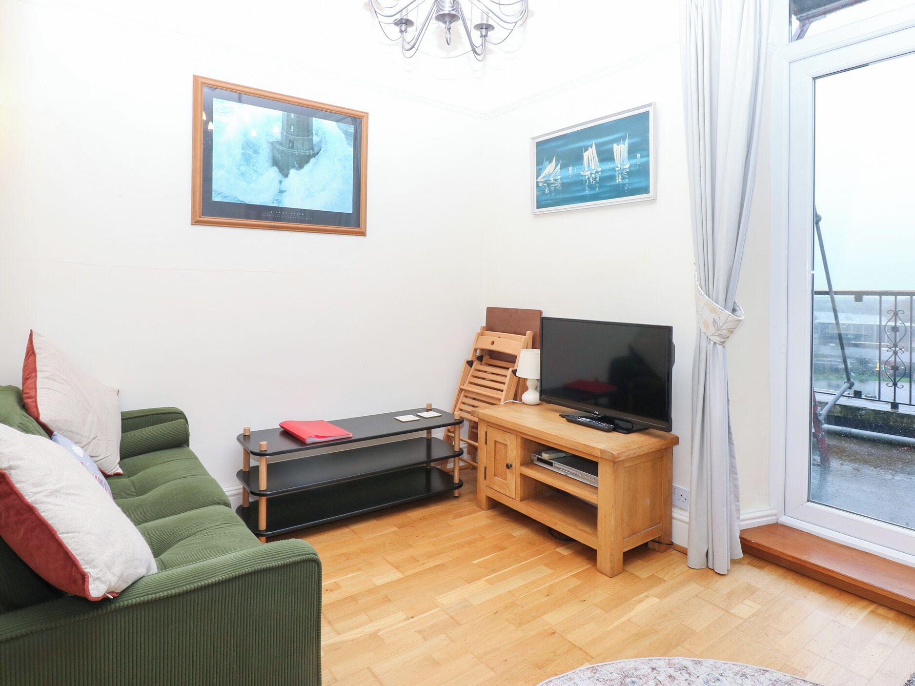 A living room with a green sofa, a wooden TV stand, a flat-screen TV, and two framed pictures on the wall.