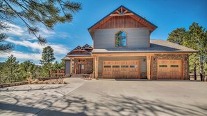 A two-story house with a stone foundation, a large garage, and a prominent front porch. - Wolf Ridge- Deadwood South Dakota (Sturgis)