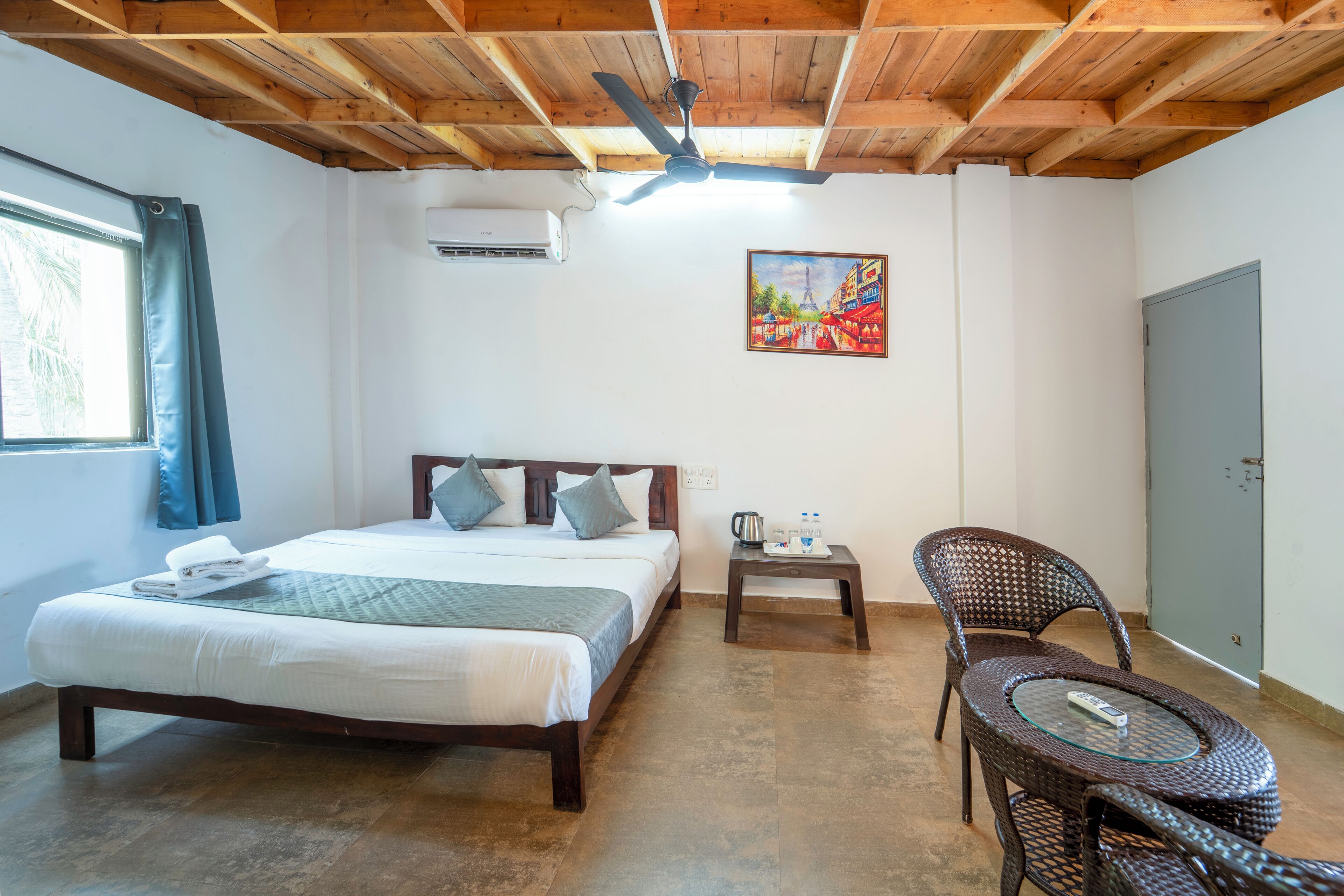 Un dormitorio con cama, una silla, una mesa, ventilador de techo, un cuadro y aire acondicionado.