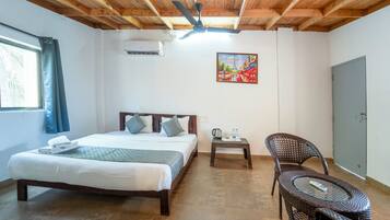 Un dormitorio con cama, una silla, una mesa, ventilador de techo, un cuadro y aire acondicionado.