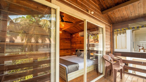 A wooden cabin with a bed, a chair, and a ceiling fan. - BeachWalk By FeatherTouch Hotels Resorts (Morjim)