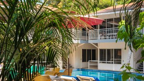 A pool area with lounge chairs, a staircase, and a balcony. - BeachWalk By FeatherTouch Hotels Resorts (Morjim)