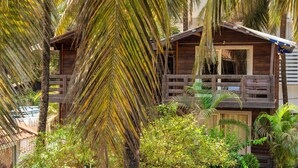 A wooden cabin with a balcony, surrounded by lush greenery and palm trees. - BeachWalk By FeatherTouch Hotels Resorts (Morjim)