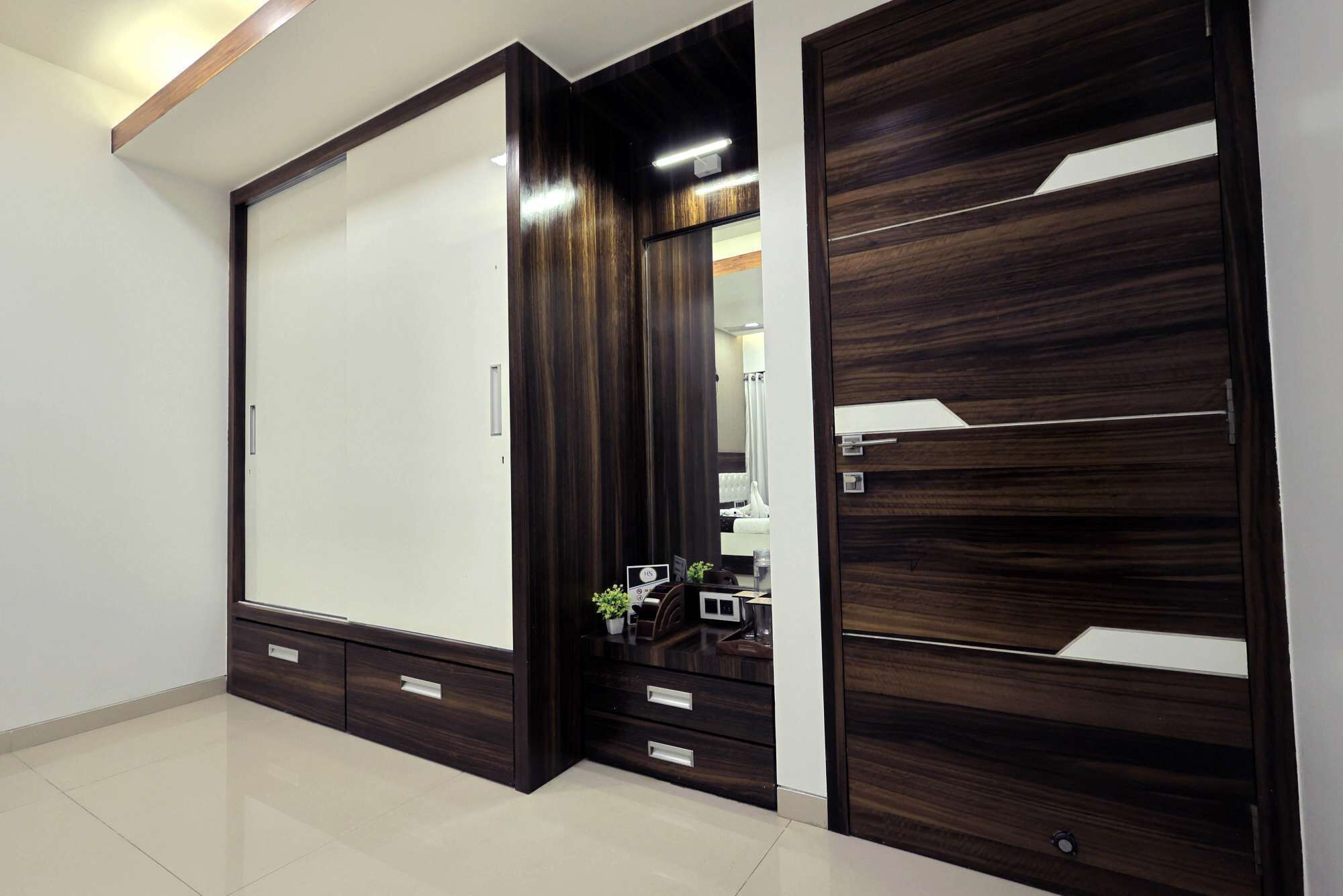 A modern wardrobe with a mirror, a small plant, and a nightstand with a lamp.