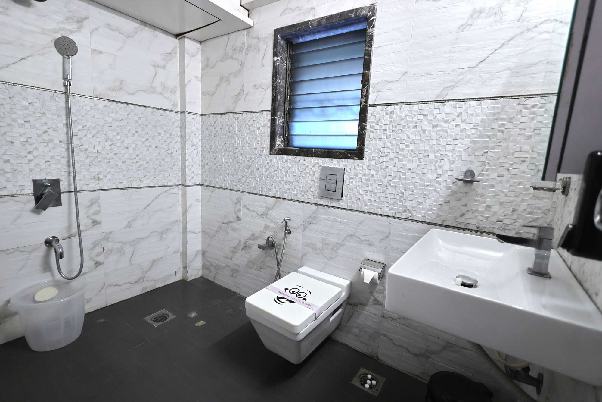 A bathroom with a shower, toilet, and sink, featuring marble walls and a small window.