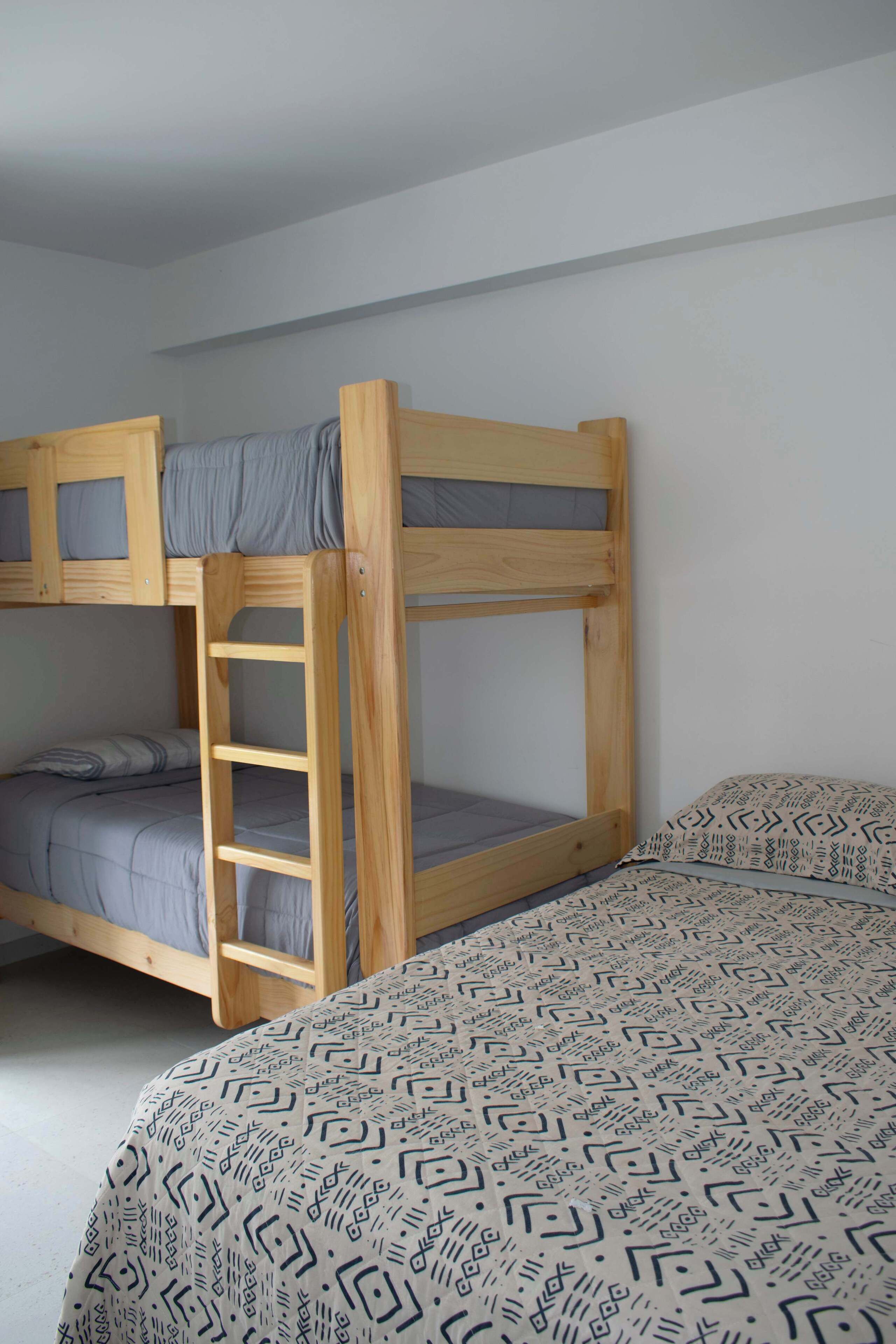 Een stapelbed met een ladder, een onderbed met beddengoed met een patroon, en een effen muur.