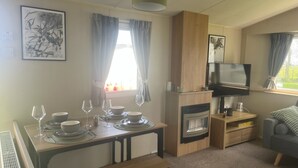 A compact living space with a dining area, a TV mounted on a wooden cabinet, a sofa, and a fireplace.