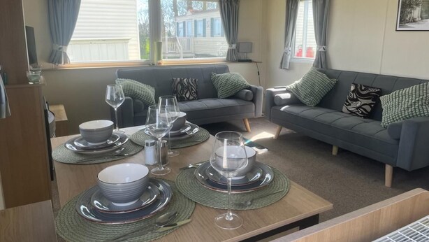 A modern living room with a dining area set for a meal, featuring a sofa, a table with plates and glasses, and a view of the outside.