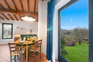 A dining area with a wooden table, chairs, and a view of a green landscape through a glass door. - Relaxing Tuscan Country Near Florence 4shared Pool (Impruneta)