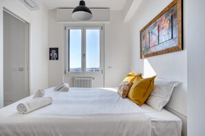 A bedroom with a bed, a window, a radiator, a painting, and a door.