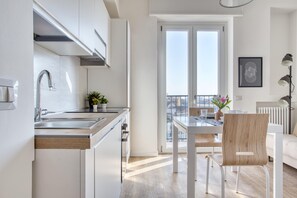 A modern kitchen with a built-in oven, a dining area with a wooden chair, and a view through a glass door to an outdoor balcony. - Bright flat near Lambretta Park (Milan)