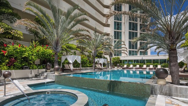 Zona de piscina con jacuzzi, sillones reclinables y palmeras.