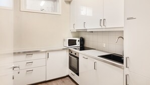 Una cocina compacta con armarios blancos, microondas, horno y lavabo.
