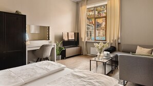 Habitación de hotel con cama, escritorio con computadora, televisor, sofá y ventana con vista a la ciudad.
