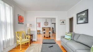 Sala de estar com sofá, poltrona, mesa de centro e um espaço de jantar ao fundo.