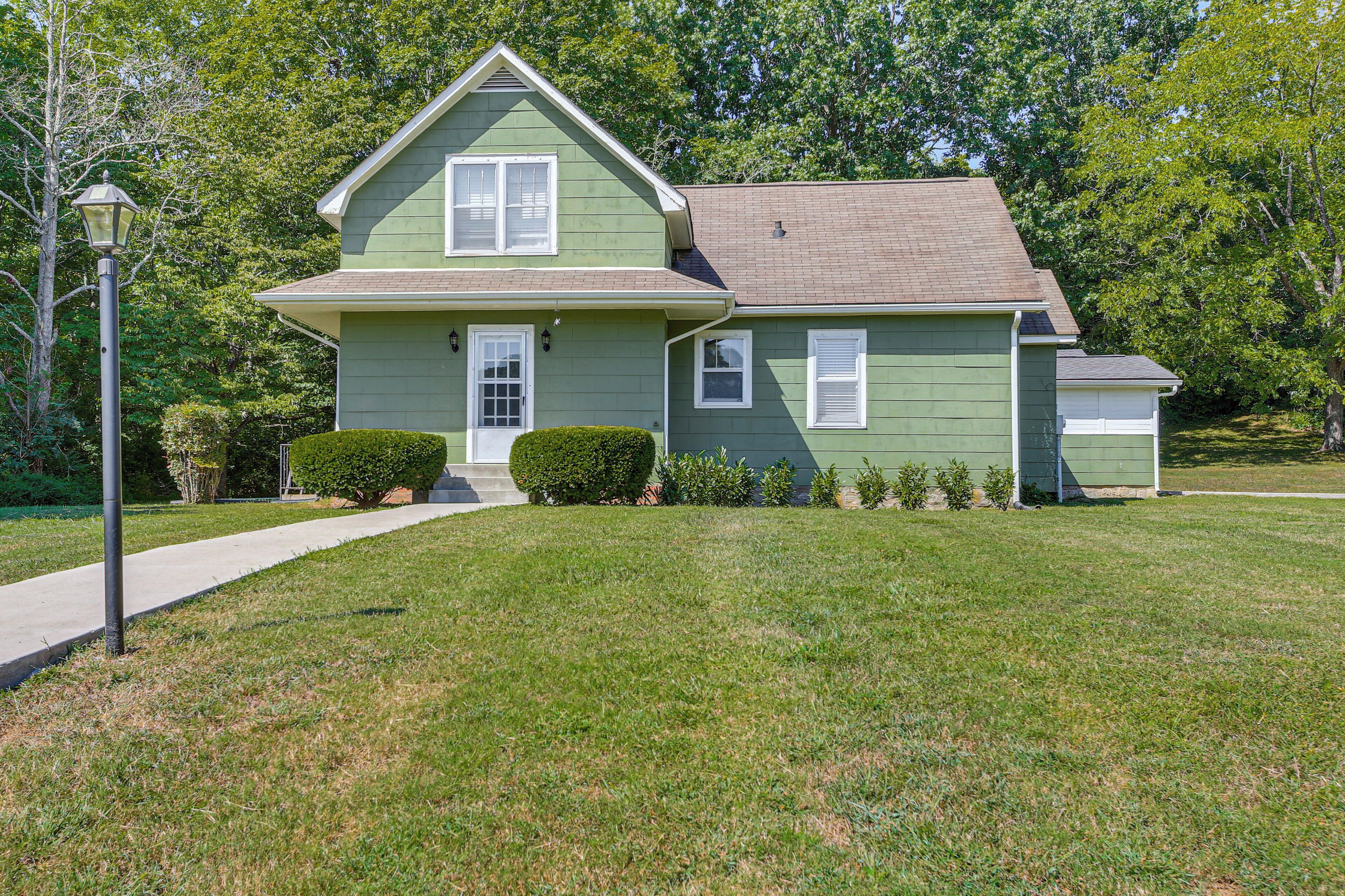 A green two-story house with a front porch, a small garage, and a well-maintained lawn.