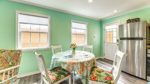 A dining area with a round table, floral tablecloth, white chairs, and a refrigerator. - Walk to Pier & Dining: Central Rockport Cottage (Rockport)