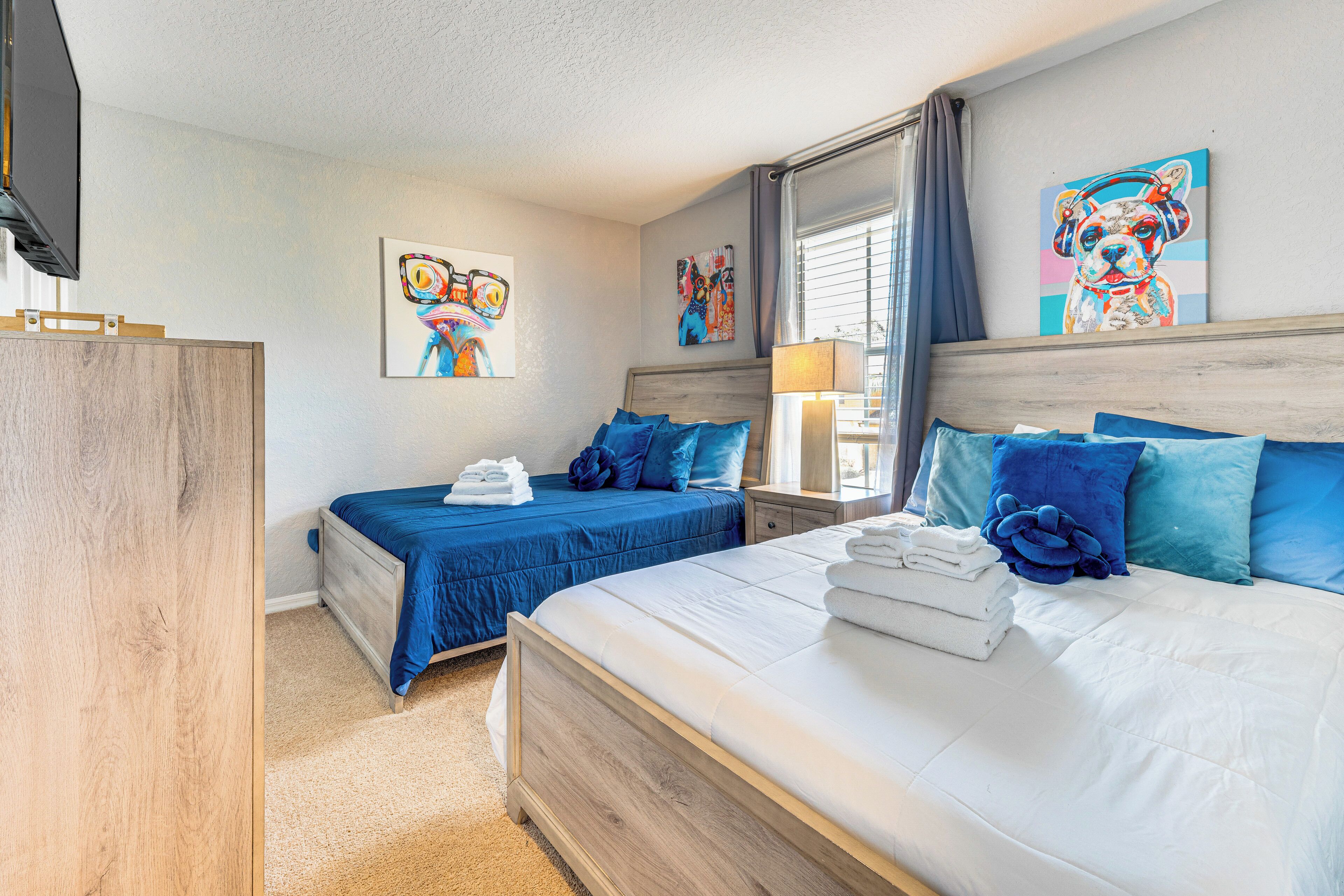 A hotel room with two beds, a wooden wardrobe, and artwork on the walls.