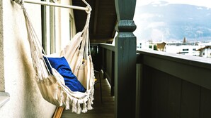 Ein Hängesessel mit blauer Sitzkissen auf einem Balkon mit Holzgeländer und Blick auf einen Berg im Hintergrund.