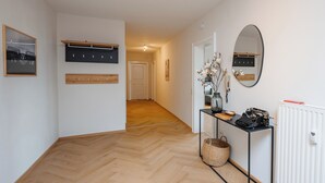 Ein Flur mit Holzboden, einem schwarzen Konsolentisch, einer Korbschale und einem Spiegel an der Wand.