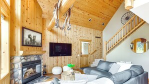 A cozy living room with a fireplace, a grey sofa, and a wooden staircase.