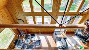 A wooden cabin with a dining area, a living room with a fireplace, and large windows offering a view of the outdoors.