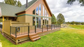 A two-story wooden cabin with a balcony, large windows, and a chimney.