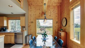 A wooden interior with a dining table, chairs, a clock, and a view of the outdoors.