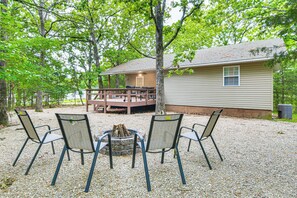 A cabin with a deck, surrounded by trees, and four chairs facing a fire pit. - Branson Area Home < 1 Mi to Table Rock Lake! (Kimberling City)