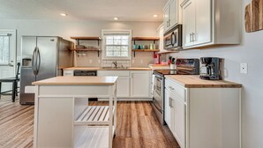 Una cocina moderna con armarios blancos, un refrigerador de acero inoxidable, un horno empotrado y una encimera de madera.