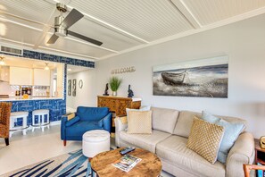 A modern living room with a blue armchair, a beige sofa, and a coffee table. A kitchen area with a bar is visible in the background. - Beach Access: Ocean-view Condo w/ Screened Balcony (Harbor Island)