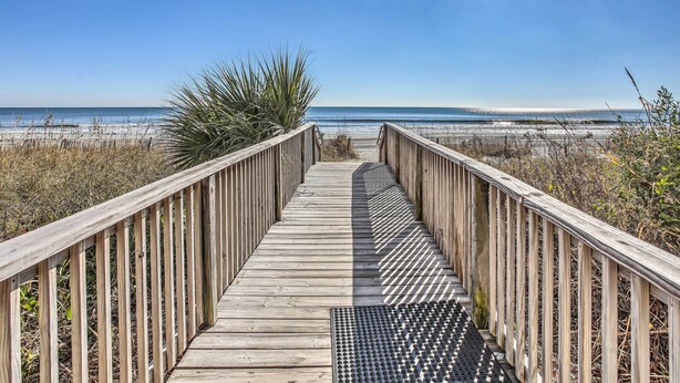 Een houten looppad dat naar een strand leidt, met een heldere lucht.