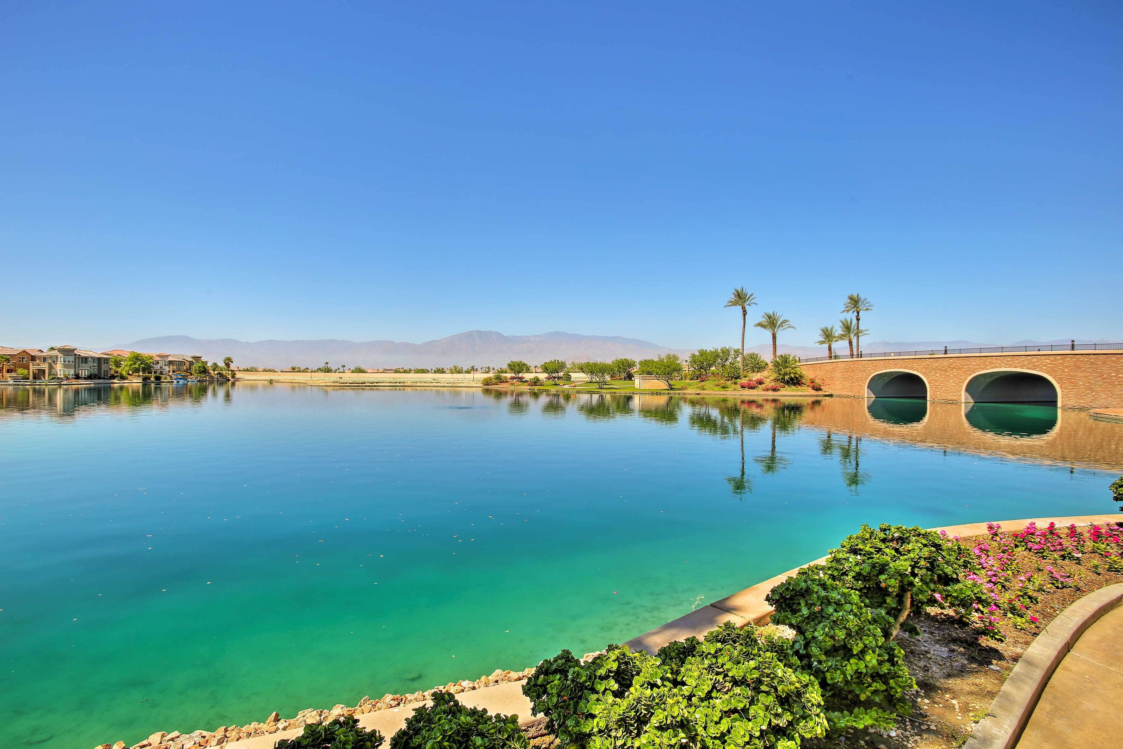 A tranquil lake with clear turquoise water, surrounded by greenery and a bridge with arches.