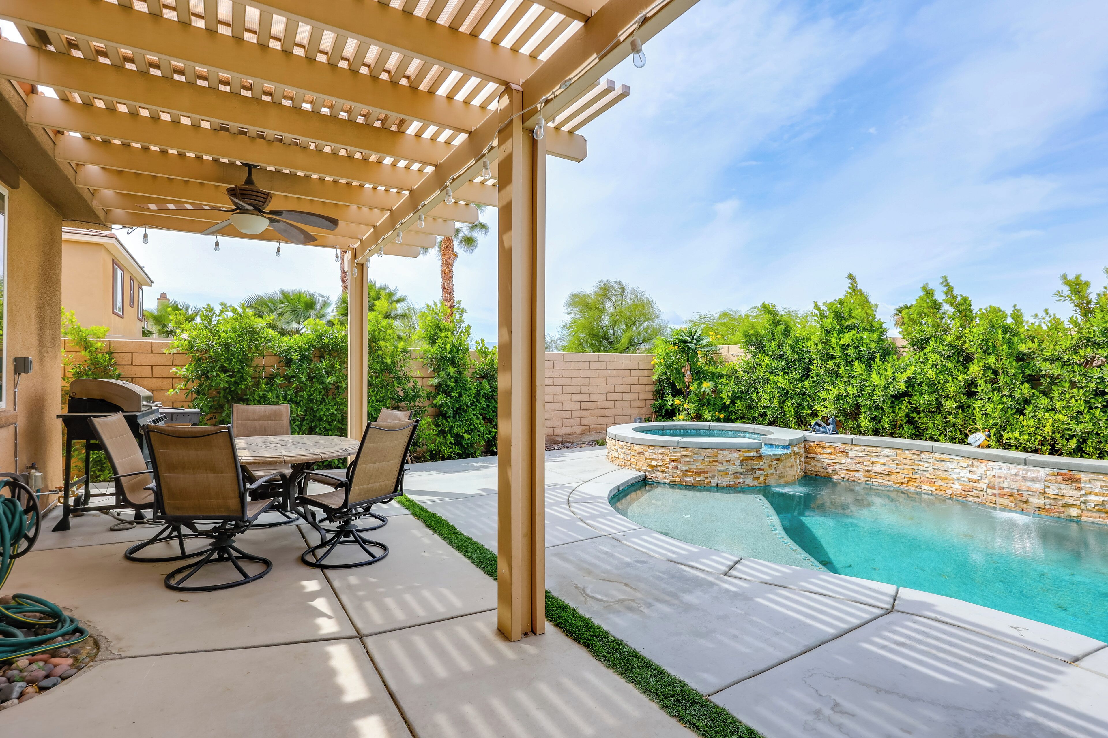 A covered patio with a pool, outdoor furniture, and a stone wall.