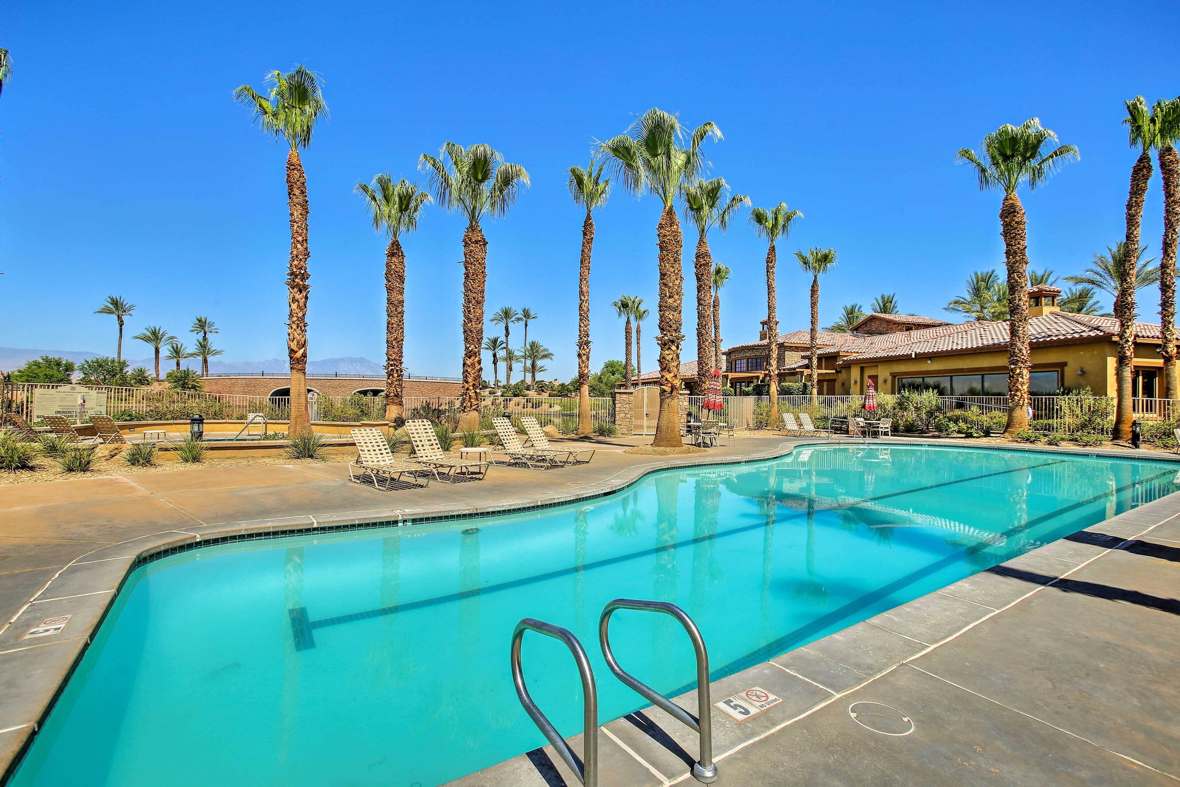 A swimming pool with palm trees, lounge chairs, and a building in the background.