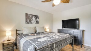 Camera da letto con un letto, comodini, una ventola a soffitto, una TV e un'opera d'arte appesa al muro.