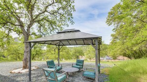 Zona relax esterna coperta con tavolo e sedie, immersa tra alberi e ghiaia.
