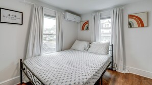 A bedroom with a bed, white curtains, an air conditioning unit, and two wall art pieces. - Walkable Dtwn Townhome Near Campus & Palmer Square (Princeton)