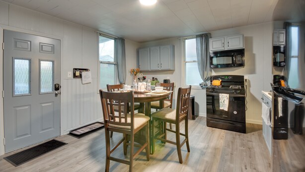 Une cuisine moderne avec des meubles en bois, une table à manger avec des chaises, un poêle noir et un four à micro-ondes.
