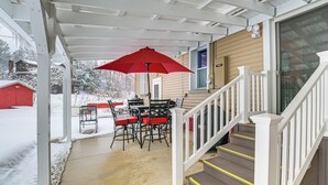 A covered porch with a red umbrella, a table with chairs, and a staircase leading to a house. - Walk to Lake Huron Beaches: Home w/ Fire Pit! (Rogers City)