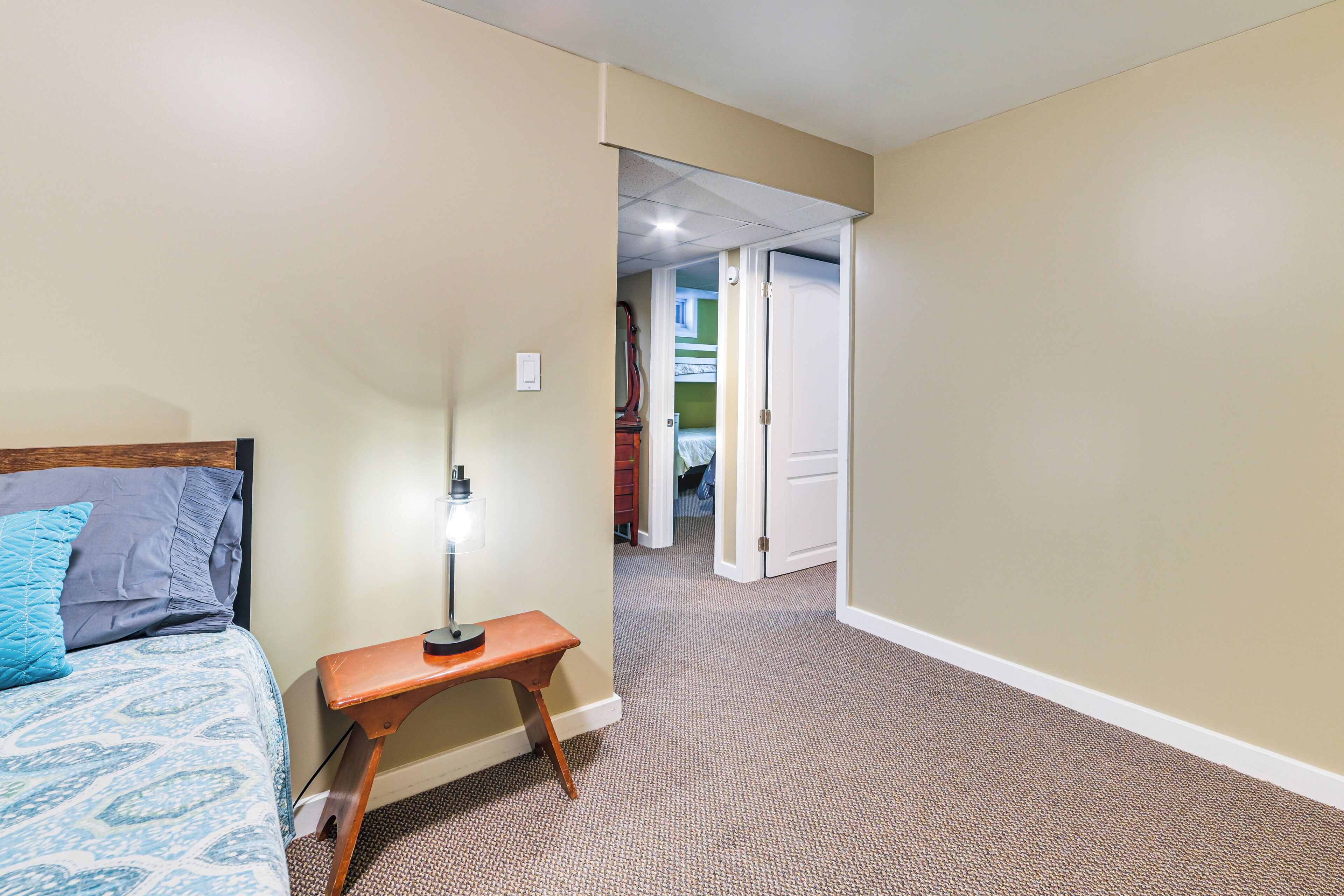 A bedroom with a bed, a nightstand, and a lamp. There is a door leading to another room.