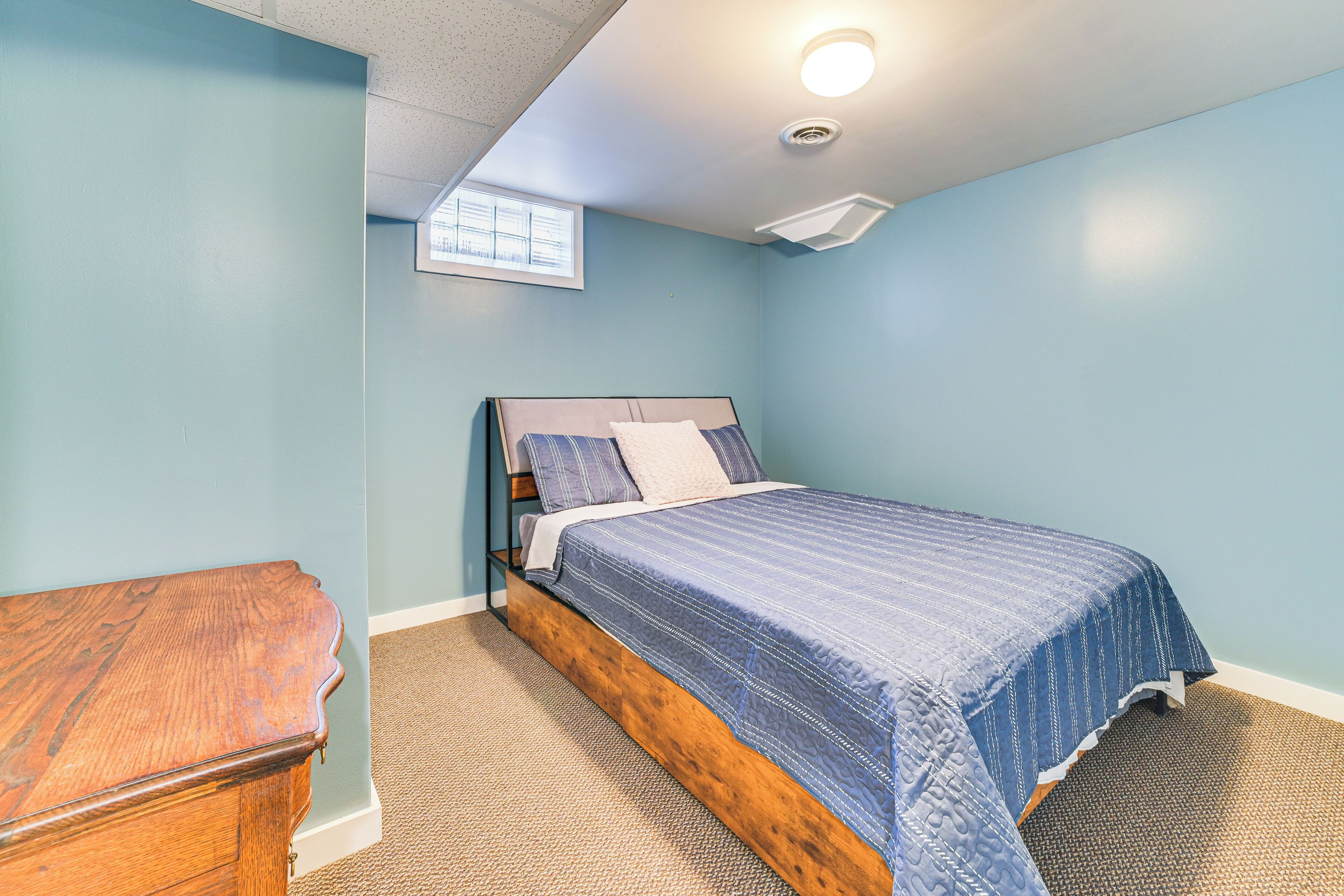 A bedroom with a bed, a wooden dresser, and a window.