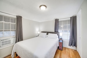 A neatly arranged bedroom with a large bed, a nightstand, a lamp, and a window with curtains. - 2 Mi to Lake Erie: Home w/ Yard in Euclid! (Euclid)