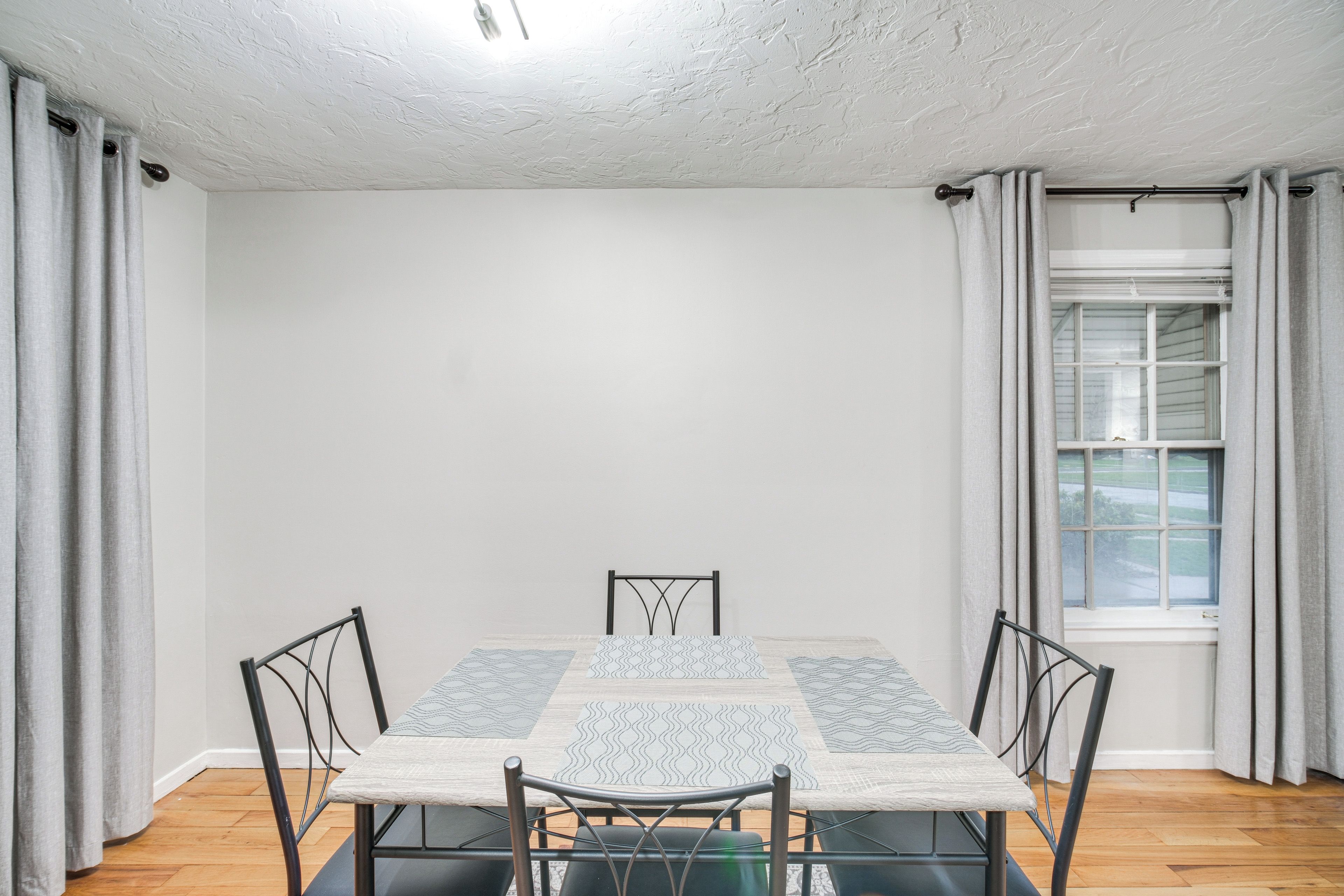 A dining room with a table and chairs, a window with curtains, and a white ceiling.