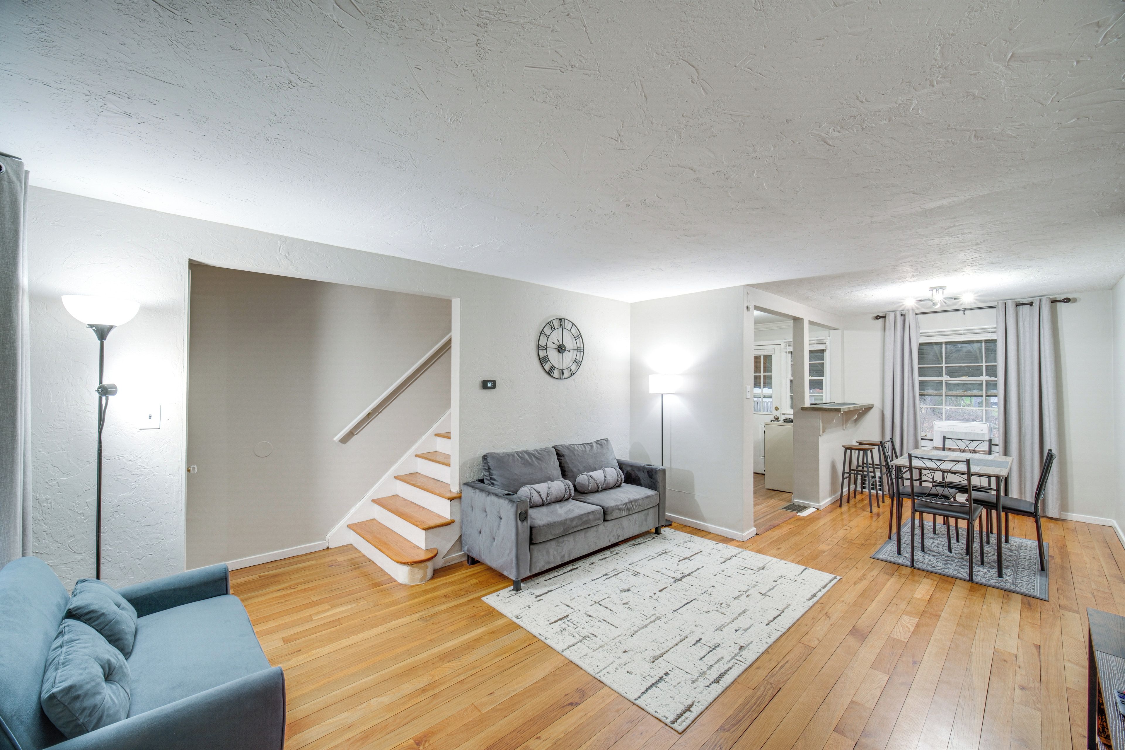 A spacious living area with a grey sofa, wooden flooring, a staircase, and a dining area with a table and chairs.