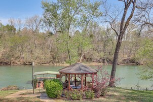 A gazebo with a roof and a covered area, surrounded by trees and a body of water.