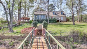 A wooden bridge leading to a house with a fenced yard and a gazebo. - Private Dock: 'the River House' in Heber Springs! (Heber Springs)