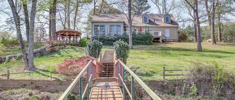 Un pont en bois menant à une maison dotée d’une cour clôturée et d’un belvédère.