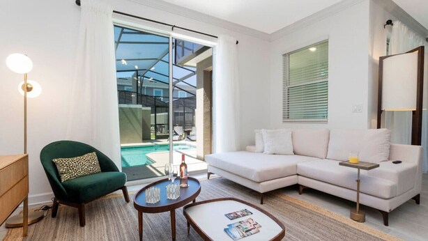 Un salon moderne avec un fauteuil vert, un canapé blanc, une table basse et une porte en verre donnant sur une piscine.