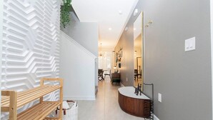 Un couloir moderne avec un banc en bois, un panier en osier blanc et une coiffeuse en bois aux lignes courbes, agrémentée d’un miroir.